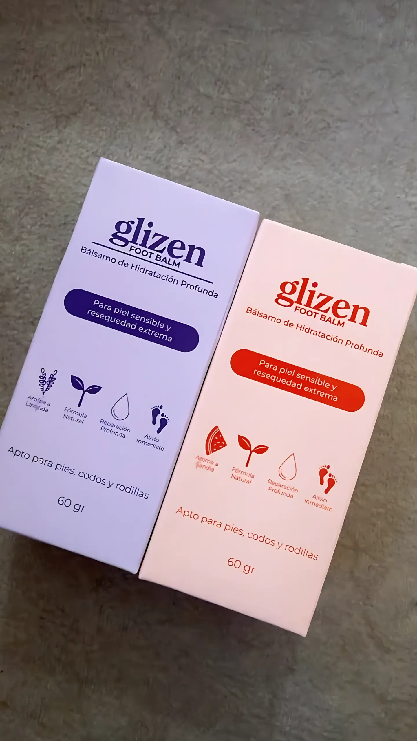 Dos cajas rectangulares de bálsamo para pies de 60 g colocadas sobre superficie gris; una morada de lavanda y otra rosada de sandía.