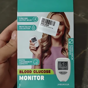 Caja de glucometro digital con pantalla grande, mostrando dispositivo blanco y lector de gota de sangre en mano de mujer sonriente.
