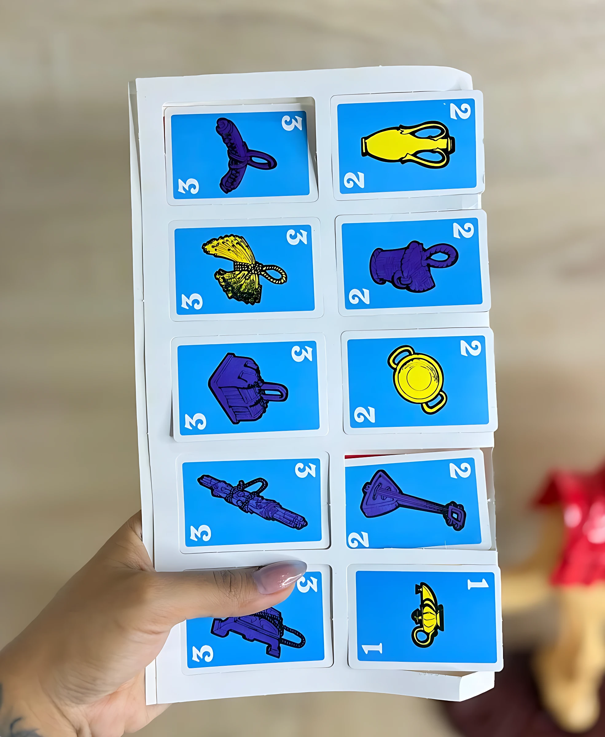 Juego de mesa familiar con cartas ilustradas de objetos variados, como camello, botella y herramientas, en colores vivos sobre fondo azul.