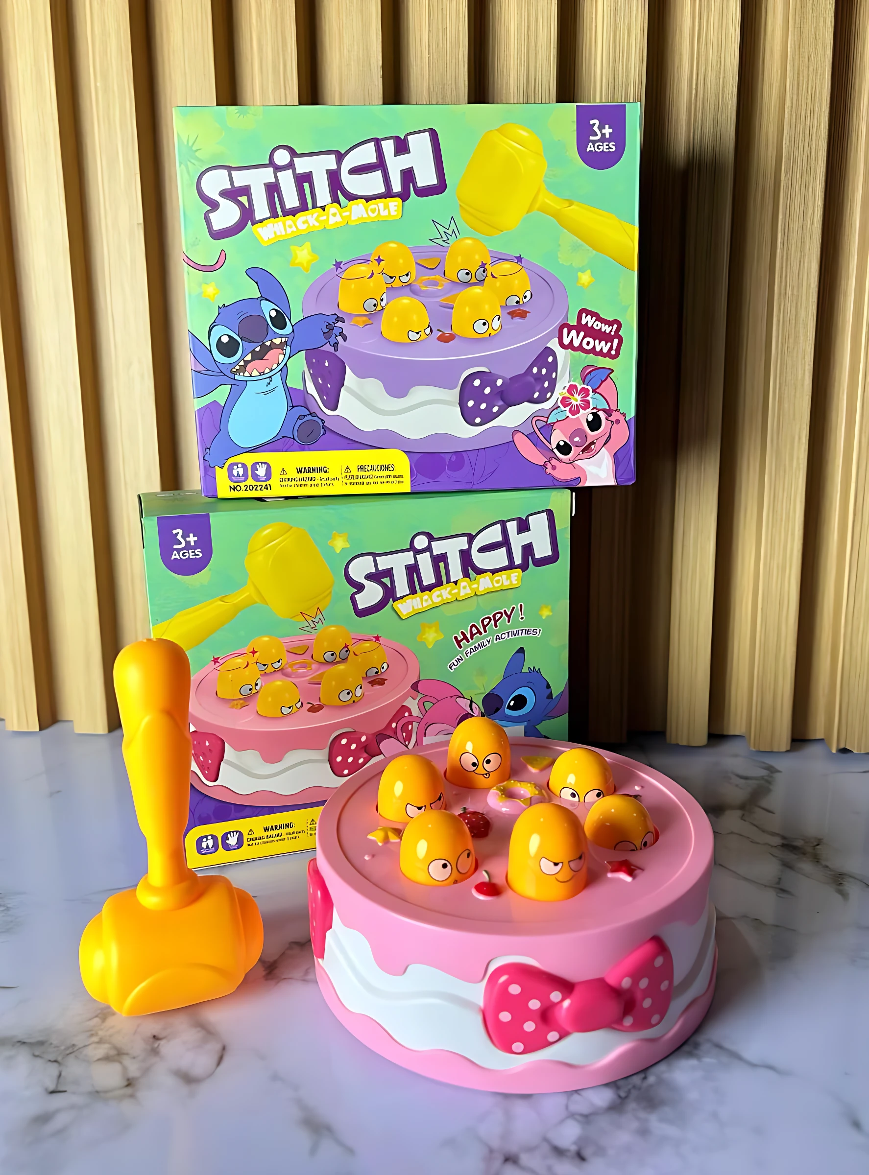 Juego Golpea el Topo Stitch en color rosa, con topo amarillo y martillo amarillo, mostrando variante Happy; incluye dos figuras de Stitch en cajas traseras.