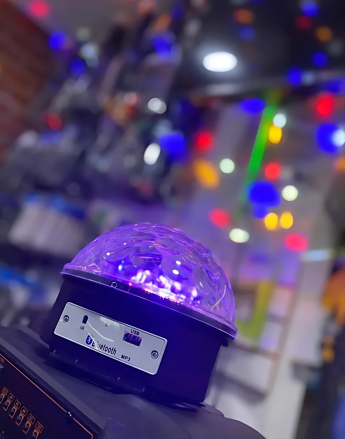 Proyector de luz disco LED con cúpula transparente y base negra, emitiendo luz morada. Incluye panel frontal con puerto USB y logotipo Bluetooth.