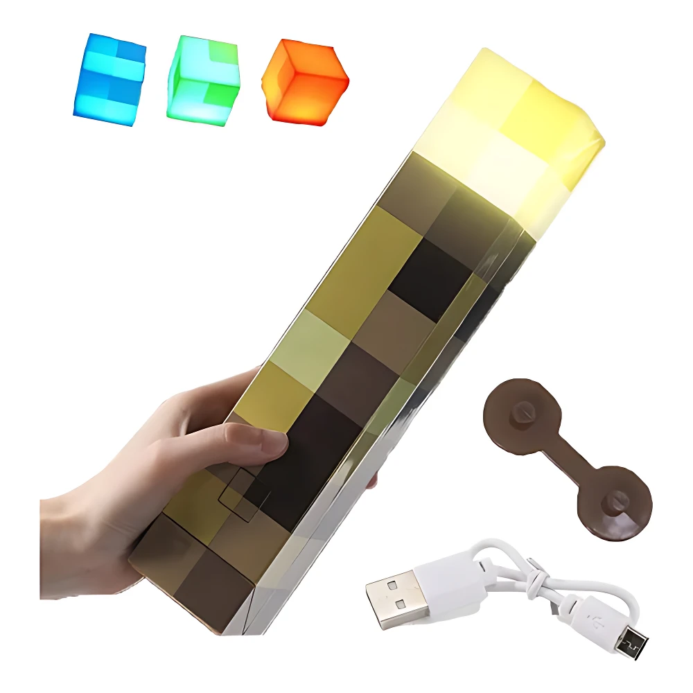 Lámpara LED rectangular con diseño pixelado de Minecraft, mostrando tonos marrones y amarillos, con luz amarilla encendida en la parte superior. Incluye tres bloques de colores (azul, verde, naranja) y accesorios USB y base magnética.