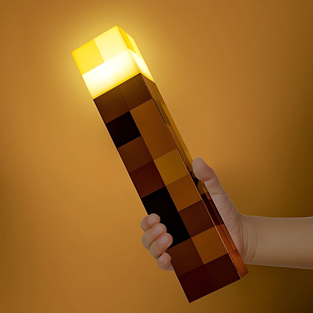 Lámpara temática Minecraft en mano, con diseño de bloque y luz amarilla encendida sobre fondo cálido.