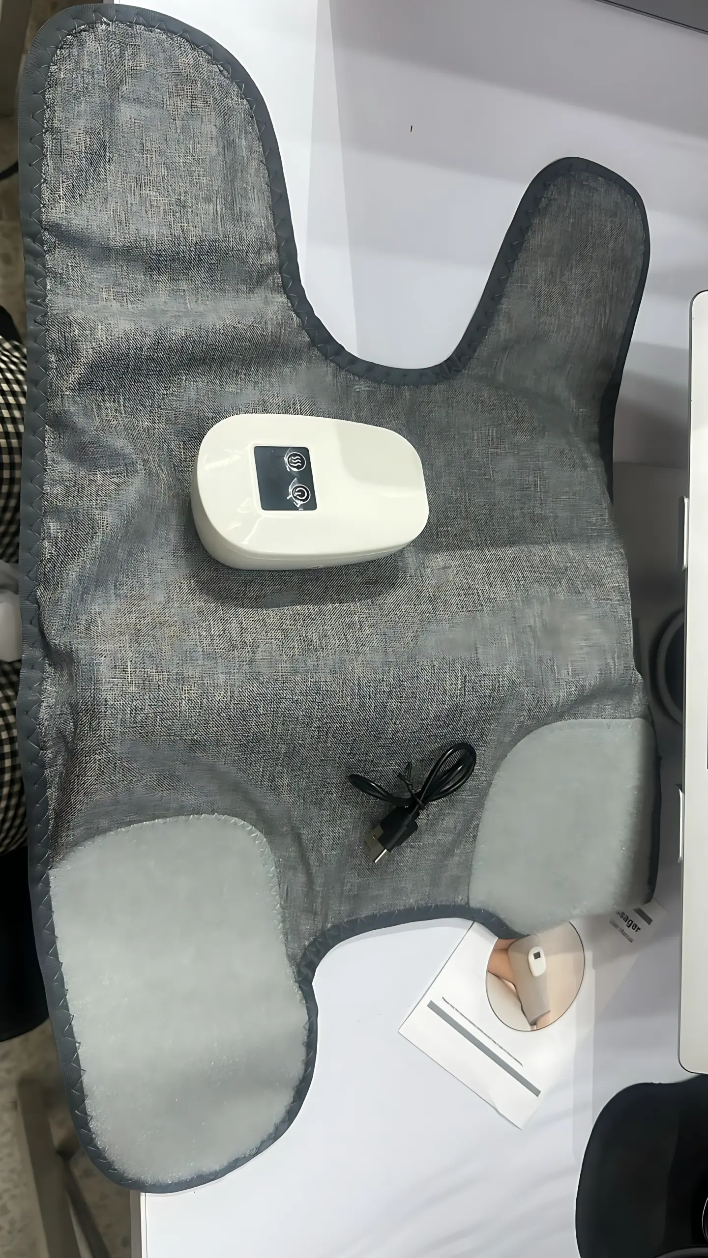 Manga de masajeador de piernas en tela gris con control remoto blanco y cable USB, diseñada para compresión de aire y calor.