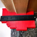 Medidor duplicador de contorno en color rojo con base de madera y regla negra con marcas de medición, colocado sobre superficie de granito.