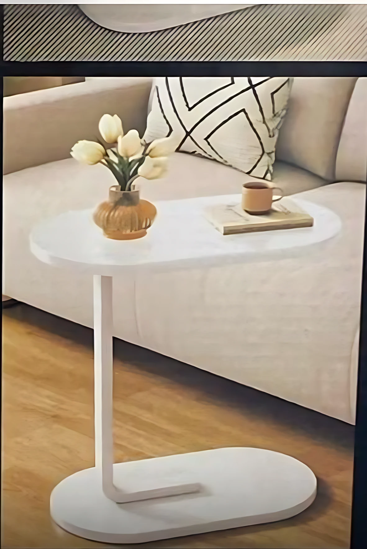 Mesa auxiliar blanca con base en forma de U, superficie redondeada y acabado liso, sobre piso de madera con sofá beige al fondo.