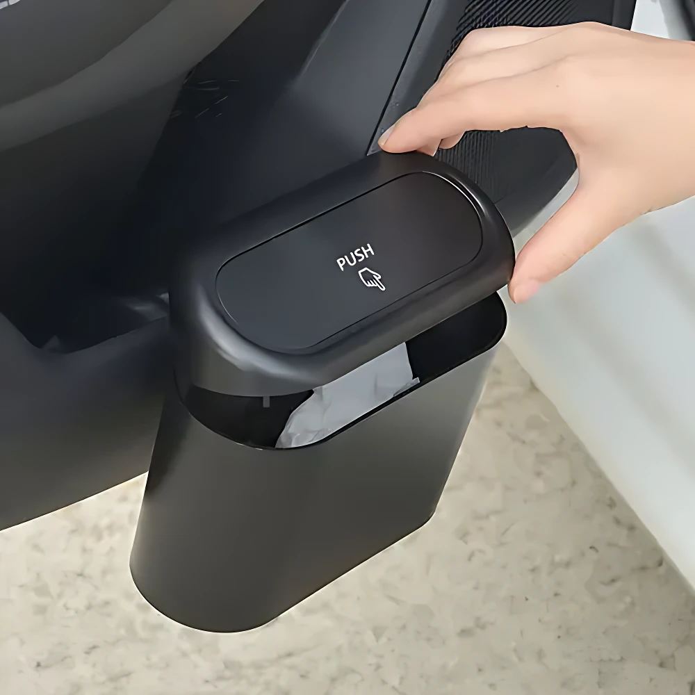 Basurero negro para carro con tapa abatible y botón PUSH, en uso dentro de vehículo.
