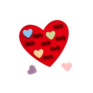 Molde de silicona rojo en forma de corazón con cavidades para chocolates, acompañado de piezas decorativas en tonos pastel.