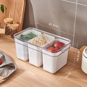 Organizador hermético de 3 divisiones transparente con medidas 27x14x14,6 cm, mostrando vegetales frescos y granos en cada compartimento sobre superficie de madera.