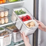 Organizador hermético de tres divisiones transparente con vegetales frescos, huevos y tubérculos en estante de refrigerador.