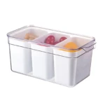 Organizador hermético transparente con tres divisiones, tapa ajustable y base blanca; contiene frutas y snacks visibles.