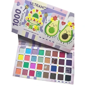 Paleta de sombras Ultramo con 32 tonos mates y brillantes, caja abierta mostrando colores vibrantes y diseños divertidos de aguacates y sombreros.