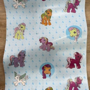 Papel adhesivo decorativo infantil con personajes de My Little Pony sobre fondo azul claro con patrones de nubes.
