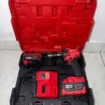 Caja roja abierta con pistola de impacto inalámbrica Milwaukee, dos baterías M18, cargador y accesorios, sobre fondo blanco.