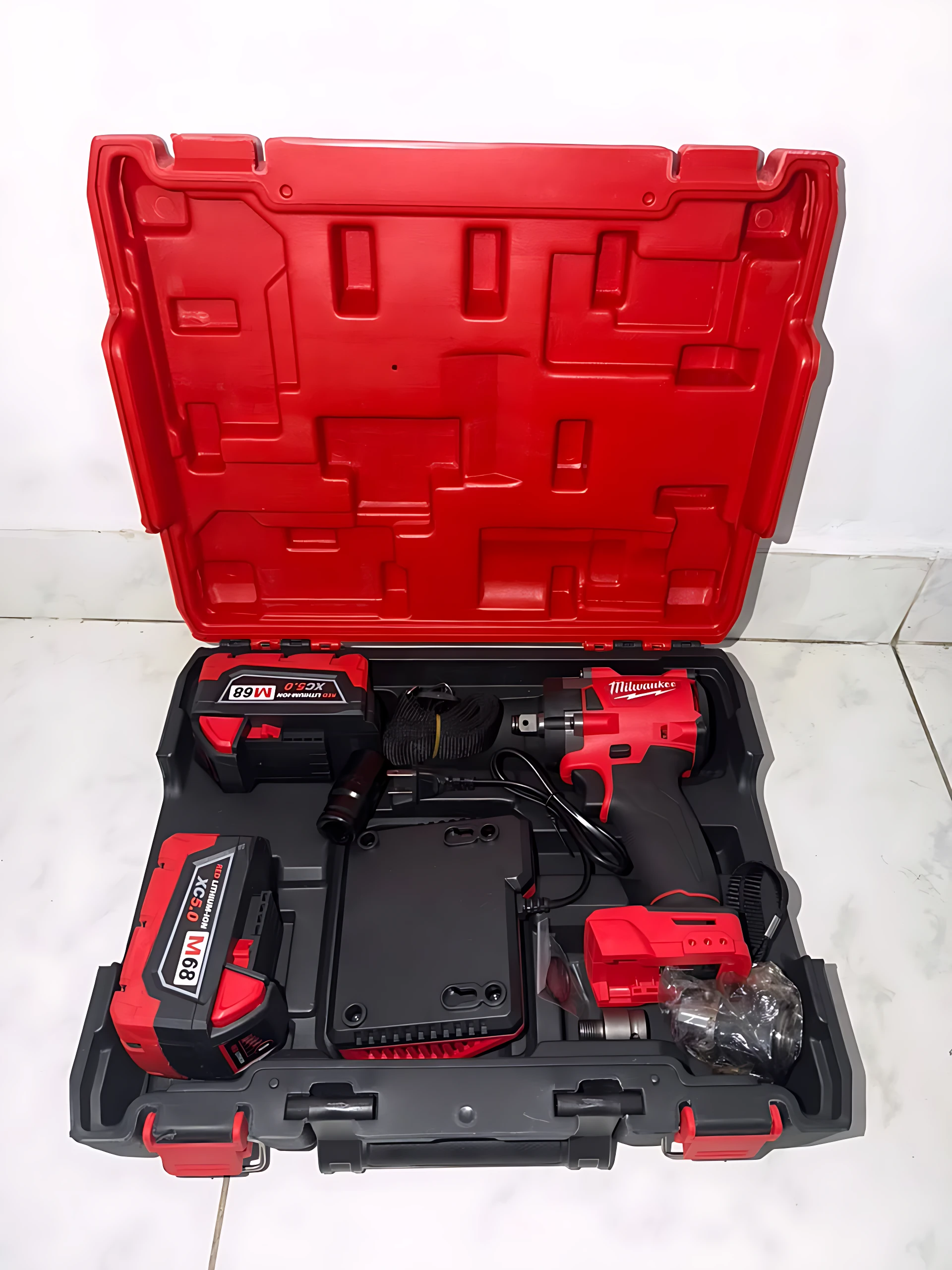 Caja abierta de color rojo con herramientas inalámbricas Milwaukee: pistola de impacto, dos baterías recargables y cargador, dispuestas en compartimentos organizados.