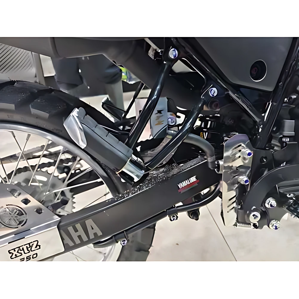 Protector bomba freno trasero Xtz 250 en acero inoxidable, montado en chasis negro con detalles cromados y logotipos visibles, diseñado para proteger contra impactos y corrosión.