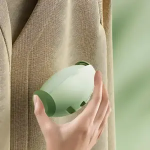 Mano sosteniendo quitamotas ergonómico en color verde claro, deslizándose sobre tela beige con textura visible, eliminando pelusas de prendas delicadas.