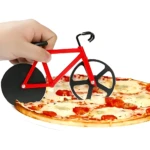 Cortador de pizza en forma de bicicleta roja con ruedas negras, siendo usado sobre una pizza de tomate y queso.