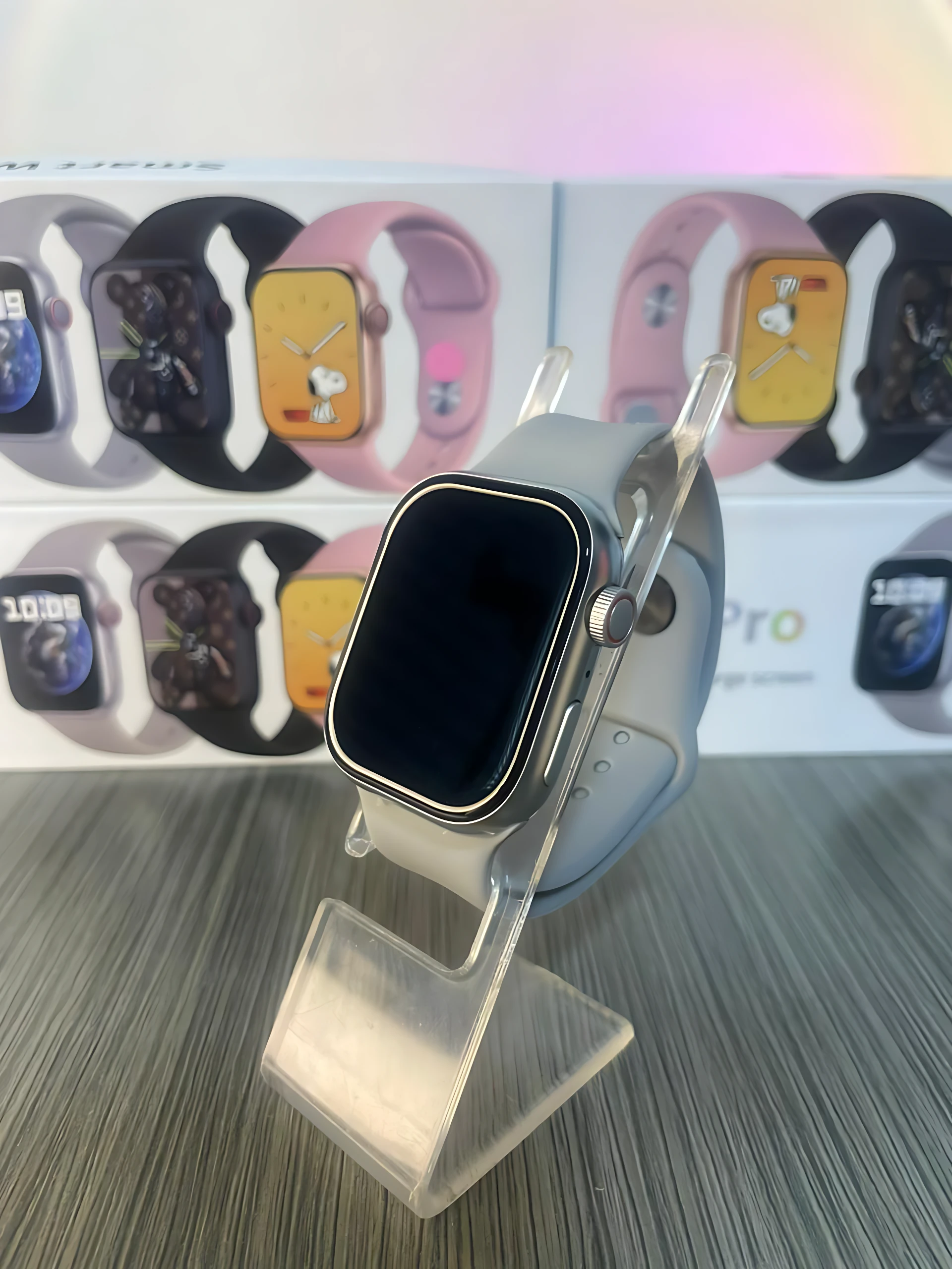 Reloj inteligente S9 Pro en color gris claro, con correa de silicona y pantalla apagada, exhibido sobre soporte transparente. Caja de presentación visible al fondo.