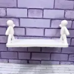 Repisa blanca con dos figuras humanas de estilo minimalista, montada sobre pared de ladrillo pintado en tono lila.