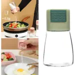 Salero de vidrio con tapa verde y medidor de gramos, mostrando uso en cocina para sazonar vegetales y huevo.