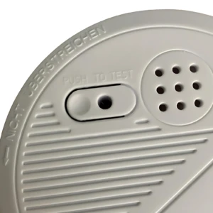 Sensor de humo fotoeléctrico blanco con botón de prueba y rejilla de sonido, detalle superior con texto en alemán y ranuras de ventilación.