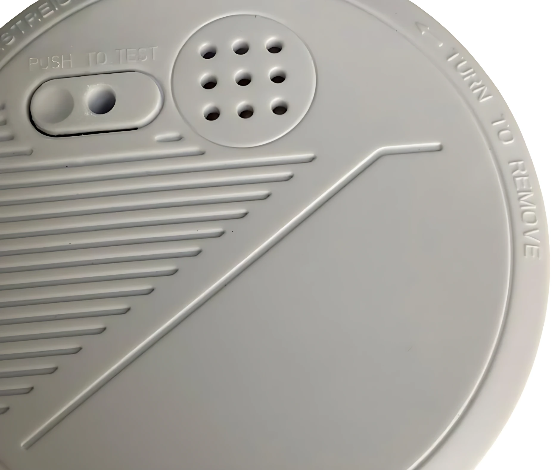 Sensor de humo fotoeléctrico gris con botón de prueba y orificios de ventilación, visto desde arriba.