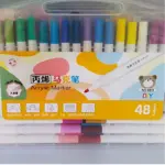 Caja transparente con 48 marcadores acrílicos de colores variados, dispuestos en dos filas horizontales. Etiqueta frontal muestra ilustraciones de uso en tela, madera y papel, junto con iconos de capacidad y resistencia al agua.