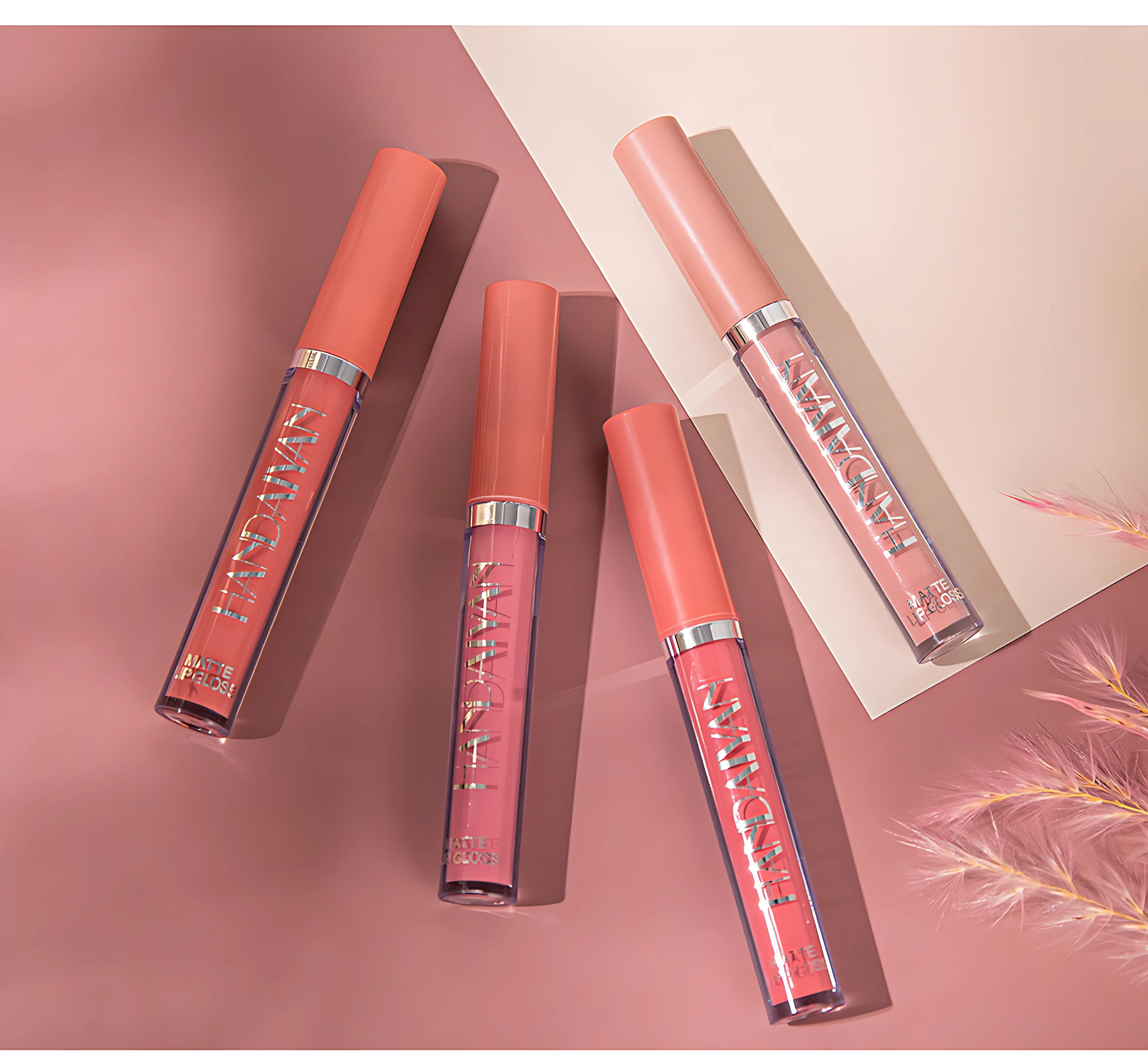 Cuatro labiales mate nude Handaiyan en tonos coral y rosa, dispuestos diagonalmente sobre fondo rosa pálido con detalles de paja decorativa.