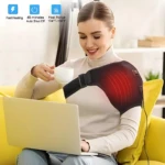 Mujer usando soporte de hombro térmico negro con zona roja de calor, sentado en sofá amarillo mientras usa laptop y sostiene taza blanca.
