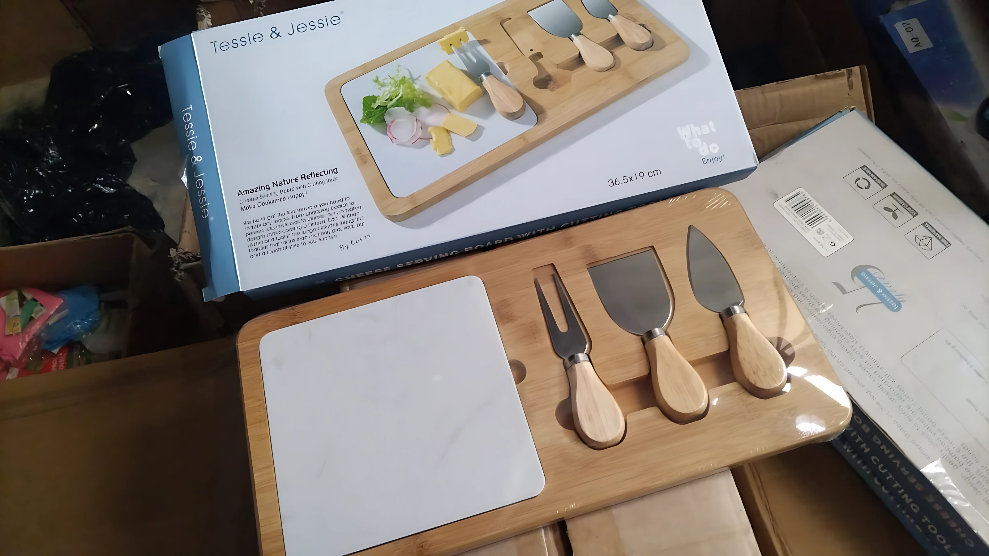 Tabla de queso cuadrada de madera con herramientas incluidas, vista frontal con caja de presentación al fondo.