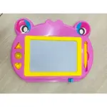 Tablero mágico de dibujo en forma de rana rosa con ojos grandes, pantalla blanca, marco amarillo y accesorios incluidos: lápiz amarillo y botones laterales.