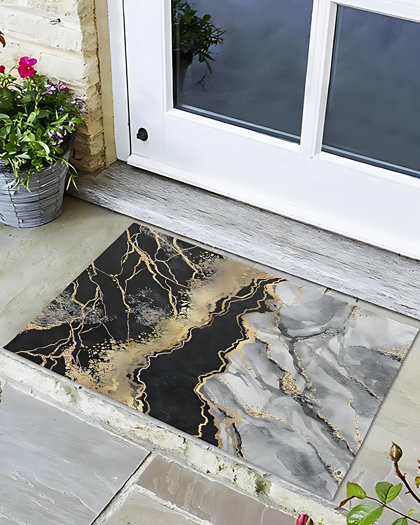 Tapete antideslizante de 30x40 cm con diseño marmolado en negro, gris y dorado, colocado frente a puerta de vidrio con marco blanco, sobre piso de baldosas grises.