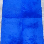 Tapete afelpado rectangular azul intenso, textura suave y larga, sobre piso de madera clara.
