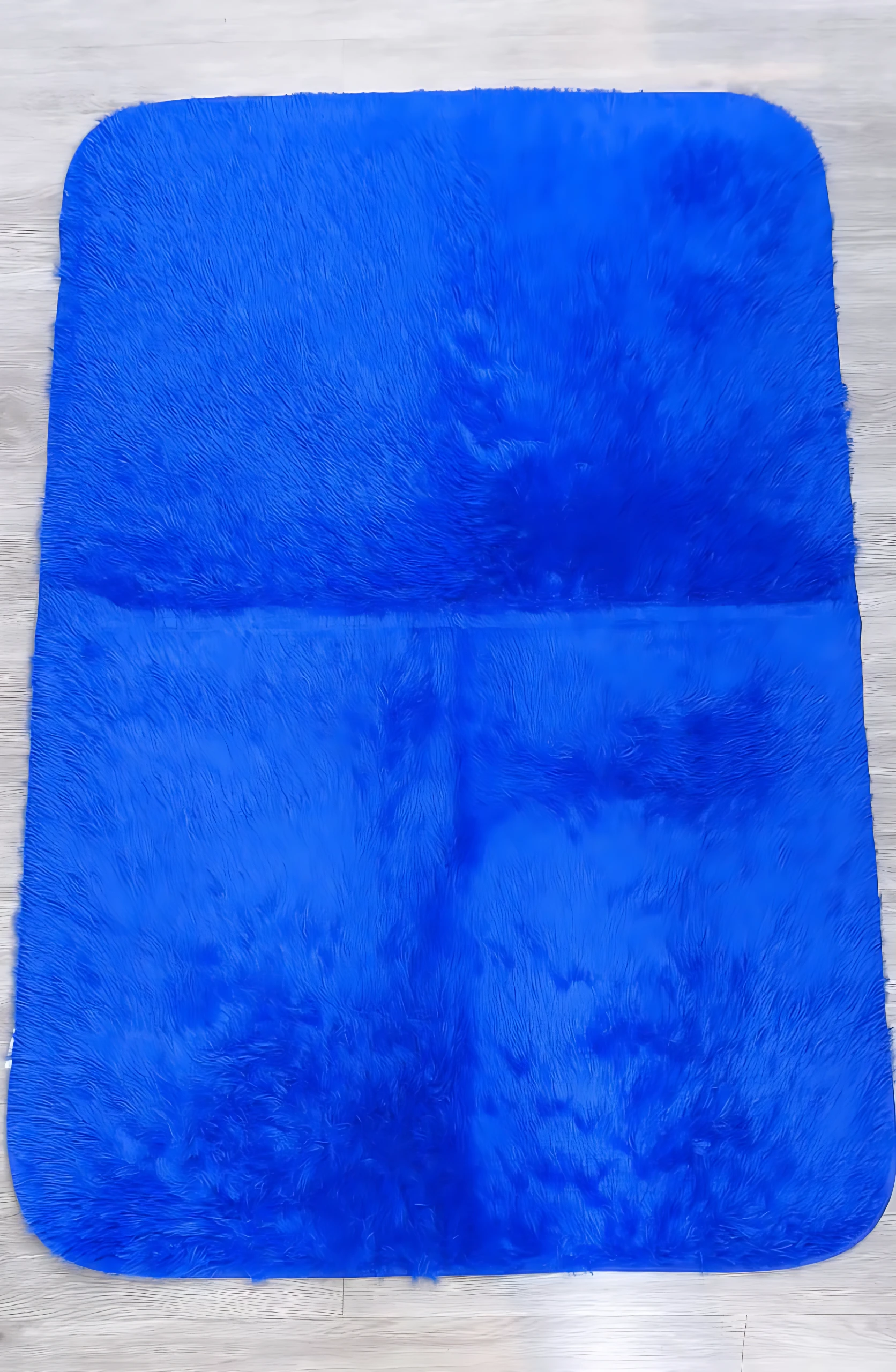 Tapete afelpado rectangular azul intenso, textura suave y larga, sobre piso de madera clara.