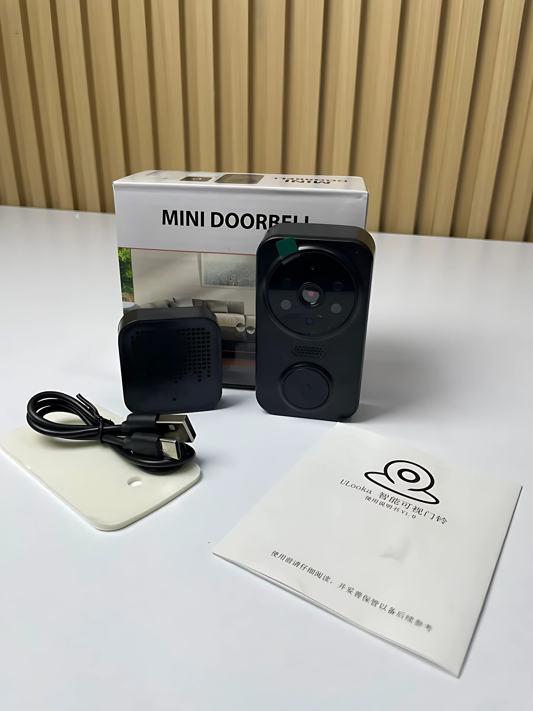 Kit de videoportero inalámbrico negro con cámara HD, timbre, cable USB, placa de montaje blanca y manual junto a su caja blanca.