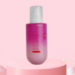Tónico facial Aghora Rosse de agua de rosas en envase degradado de magenta a rosa con dosificador blanco, sobre un pedestal y nubes rosadas.