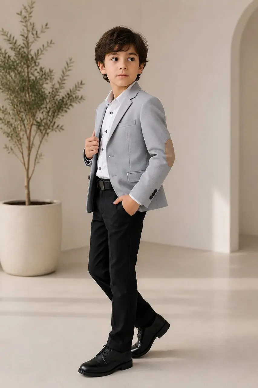 Niño vistiendo blazer gris con coderas beige, camisa blanca, pantalón y zapatos negros en espacio interior minimalista