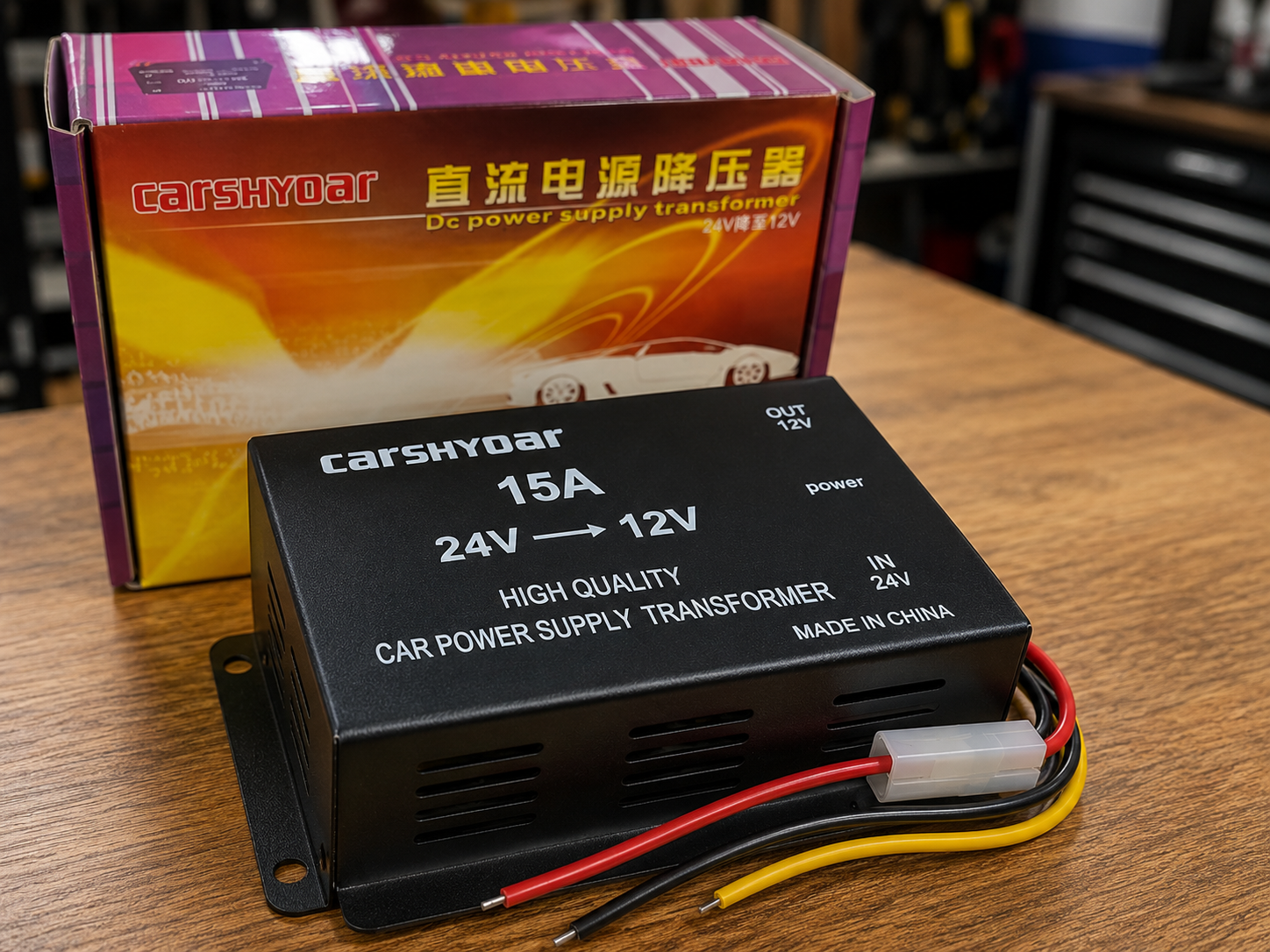 Transformador de voltaje negro 24V a 12V 15A con cables rojo, negro y amarillo, sobre mesa de madera y caja de empaque al fondo.