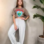 Camiseta oversize corta color café con estampado de corazón azul y coco tropical, combinada con pantalones anchos color gris claro.