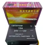 Transformador de voltaje negro CARSHYDAR 24V a 12V y 15A con su caja de empaque colorida y cables de conexión expuestos.