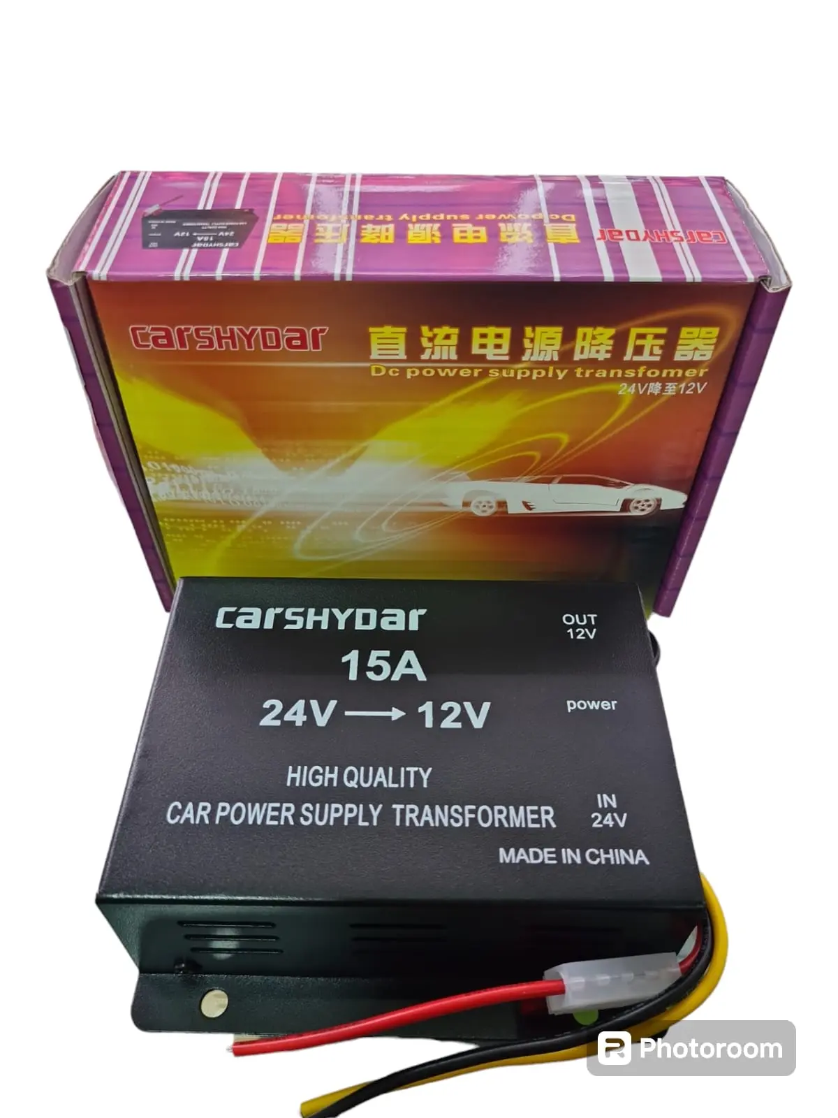 Transformador de voltaje negro CARSHYDAR 24V a 12V y 15A con su caja de empaque colorida y cables de conexión expuestos.