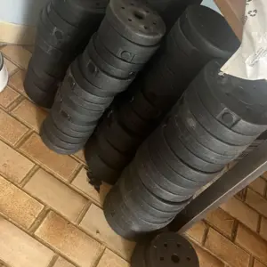Discos de pesas negros de 3 kg apilados en columnas sobre un piso de baldosas, con un disco en primer plano junto a un escritorio de madera.