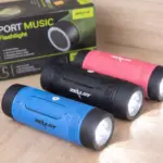 Parlantes Bluetooth Zealot S1 con linterna LED en colores azul, negro y rojo, con textura rugosa y luz encendida sobre superficie de madera.