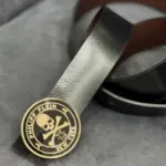 Correa de cuero negro para hombre con hebilla circular dorada con relieve de calavera y marca Philipp Plein New York.
