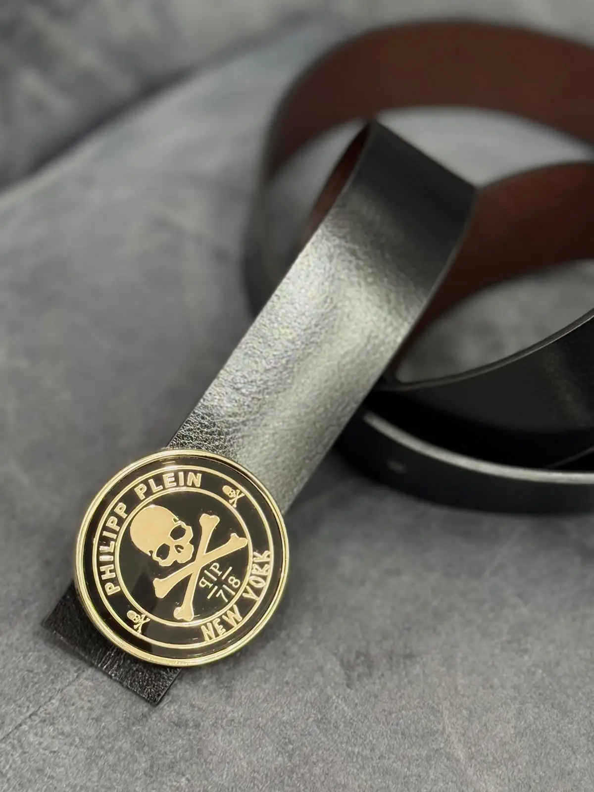 Correa de cuero negro para hombre con hebilla circular dorada con relieve de calavera y marca Philipp Plein New York.