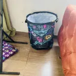 Bolsa tula grande para ropa con diseño gamer de ladrillos oscuros y luces neón de colores, ubicada en el piso junto a un sofá.