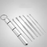 Kit de limpieza de oídos metálico plateado con estuche cilíndrico tipo llavero y seis herramientas de acero de distintas puntas y formas.