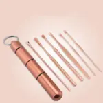 Kit de limpieza de oídos color oro rosa con estuche cilíndrico portátil y seis herramientas metálicas de diversas puntas y formas.