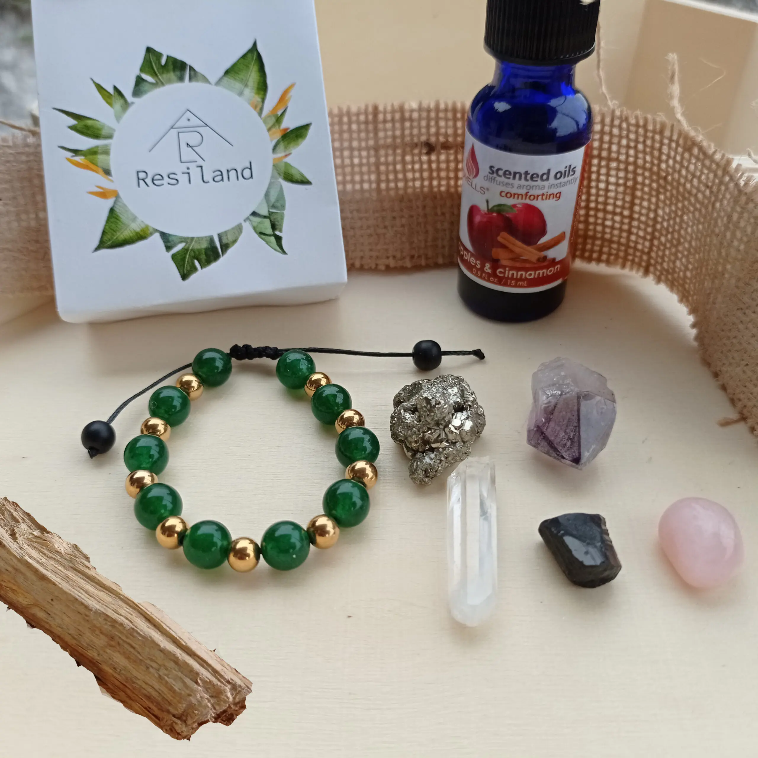 Kit energético 8 en 1 con caja Resiland, pulsera verde y dorada, aceites de manzana y canela, palo santo y cinco cristales variados.